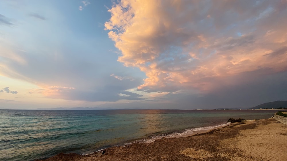 a beach with a body of water and a cloudy sky