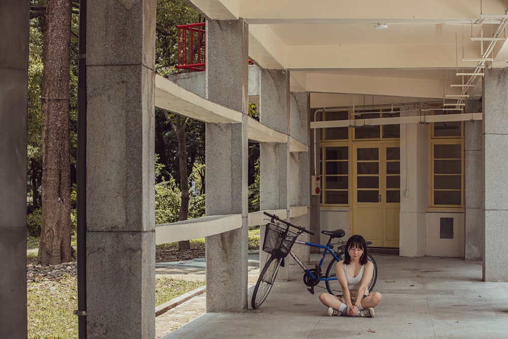 a person sitting on a sidewalk next to a bicycle