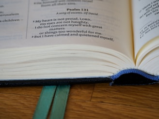 An open book with visible text from Psalm 131, featuring blue stitching along the spine and two green bookmarks underneath. The pages appear slightly yellowed, indicating a well-used or aged book.