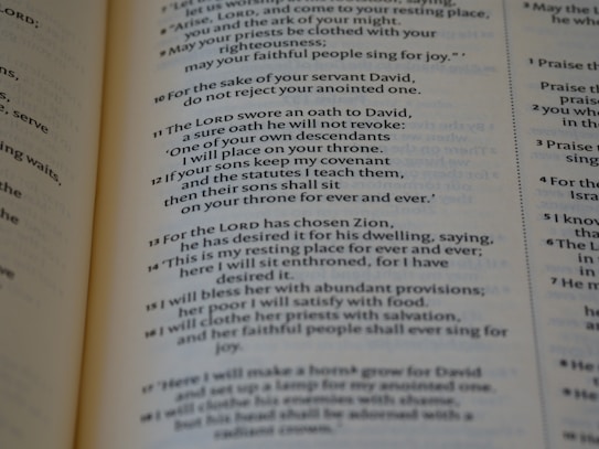 A close-up view of a page from a book displaying religious text. The text is formatted in verses, organized numerically, and printed in black ink on light-colored paper.