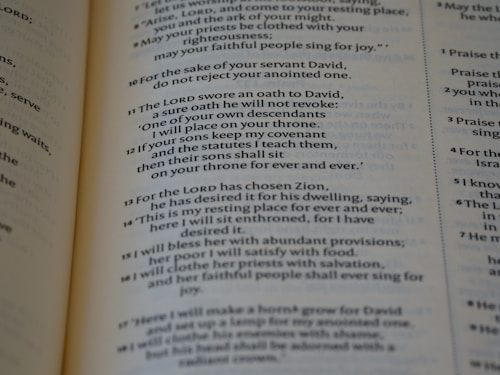 A close-up view of a page from a book displaying religious text. The text is formatted in verses, organized numerically, and printed in black ink on light-colored paper.