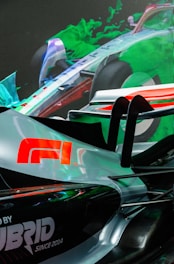 A sleek, futuristic race car design with a prominent logo and vibrant green and blue abstract shapes in the background. The car features a silver and black color scheme with red accents.