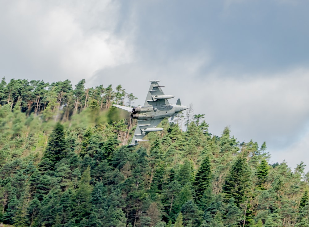 a military plane flying over trees