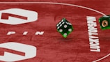 Two green dice with rounded edges are positioned on a red surface that seems to be part of a game board. The surface has white text and numbers on it, including the word 'LUCKYTOPSPIN' in capital letters.