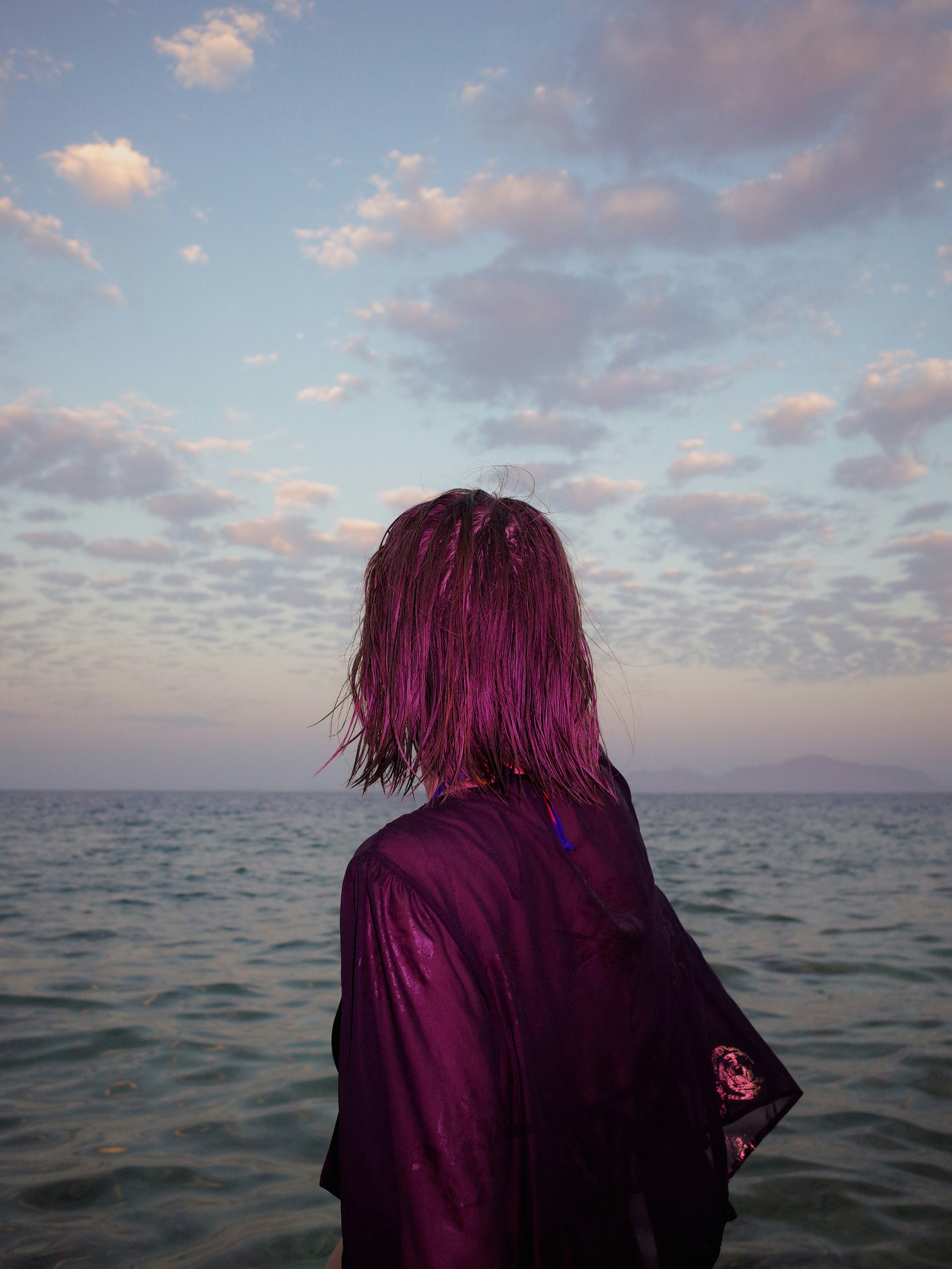 A person looks out at the sea under a sunset.