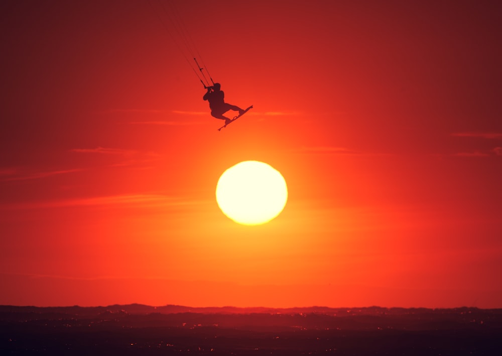 a person in the air with a parachute in front of a sunset
