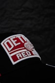 Close-up of a red embroidered logo on a black snapback hat against a dark background.