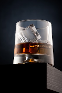 A handcrafted whiskey glass on a wooden table, filled with amber liquid and a soft glow.
