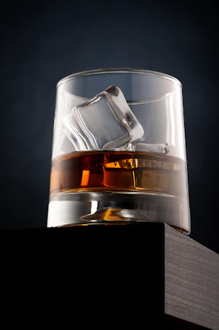 A hand placing an amber aura ice stone into a crystal whiskey glass, capturing the ritual of enjoying a fine drink.