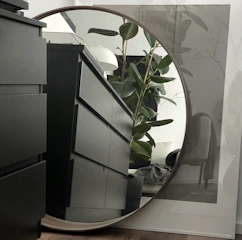 A sleek, modern minimalist dressing table with clean lines and a soft matte finish, styled with a small vase and a round mirror.