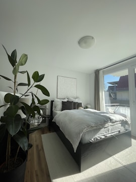 A bright master bedroom with soft linens and a large window view.