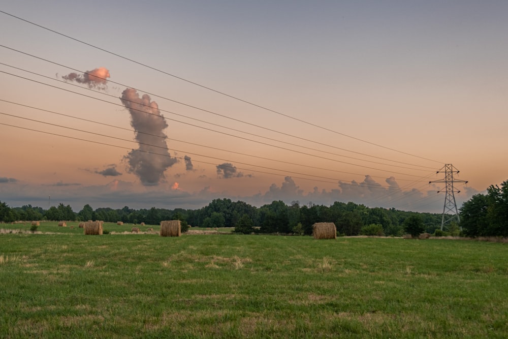 a field with hay bales and smoke stacks in the distance