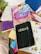 A cluttered tabletop features a variety of colorful notebooks and journals. One prominent black notebook has the word 'IDEAS' on it. Other visible items include a colorful journal with the phrase 'don't overthink it' and a remote control. Brightly colored pens are scattered among the notebooks.