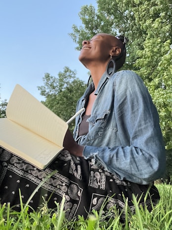 A smiling person journaling outdoors with a view of trees and fresh air.