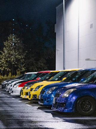 A row of rental cars in various colors lined up in a bright lot.