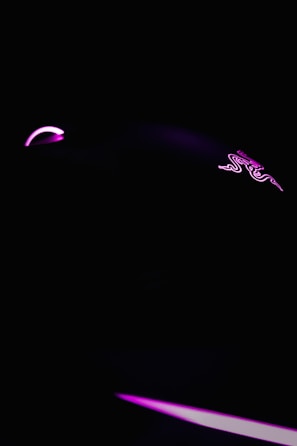 A dark, minimalist scene featuring a gaming mouse highlighted with neon pink lighting. The mouse logo is faintly visible, and the overall ambiance is sleek and futuristic.