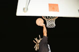 A dynamic shot of players mid-air during a slam dunk under glowing arena lights.