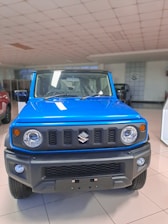 A vibrant blue SUV with a rugged front design is displayed in a well-lit showroom. The vehicle features round headlights, a bold grille with a logo, and an angular bumper. The floor is tiled, and other vehicles can be partially seen in the background.