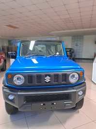 A vibrant blue SUV with a rugged front design is displayed in a well-lit showroom. The vehicle features round headlights, a bold grille with a logo, and an angular bumper. The floor is tiled, and other vehicles can be partially seen in the background.