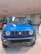 A vibrant blue SUV with a rugged front design is displayed in a well-lit showroom. The vehicle features round headlights, a bold grille with a logo, and an angular bumper. The floor is tiled, and other vehicles can be partially seen in the background.