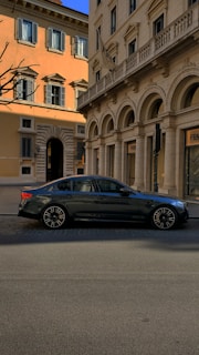 A sleek, black sedan waiting outside Rome's Fiumicino airport terminal under a bright blue sky.