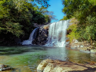 A serene Balinese waterfall surrounded by lush green rice terraces under a clear blue sky.