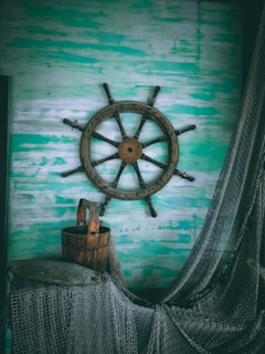 Close-up of a handcrafted wooden captain's wheel mounted on a textured wall.