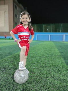 A young girl in a turquoise jersey skillfully dribbling a soccer ball on a sunlit field.
