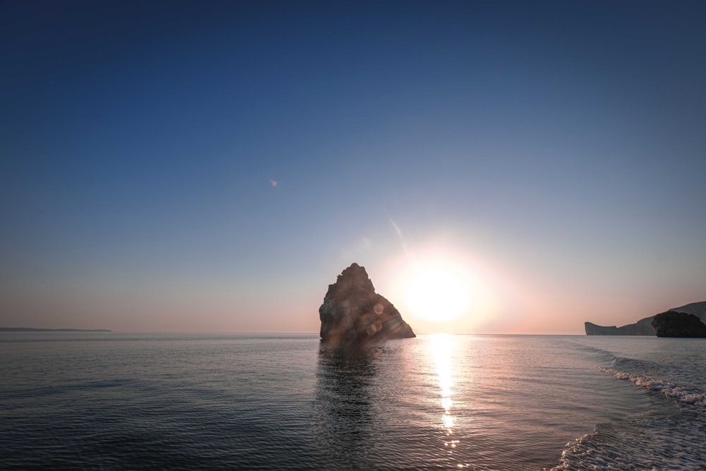 a body of water with a rock in the middle and a blue sky