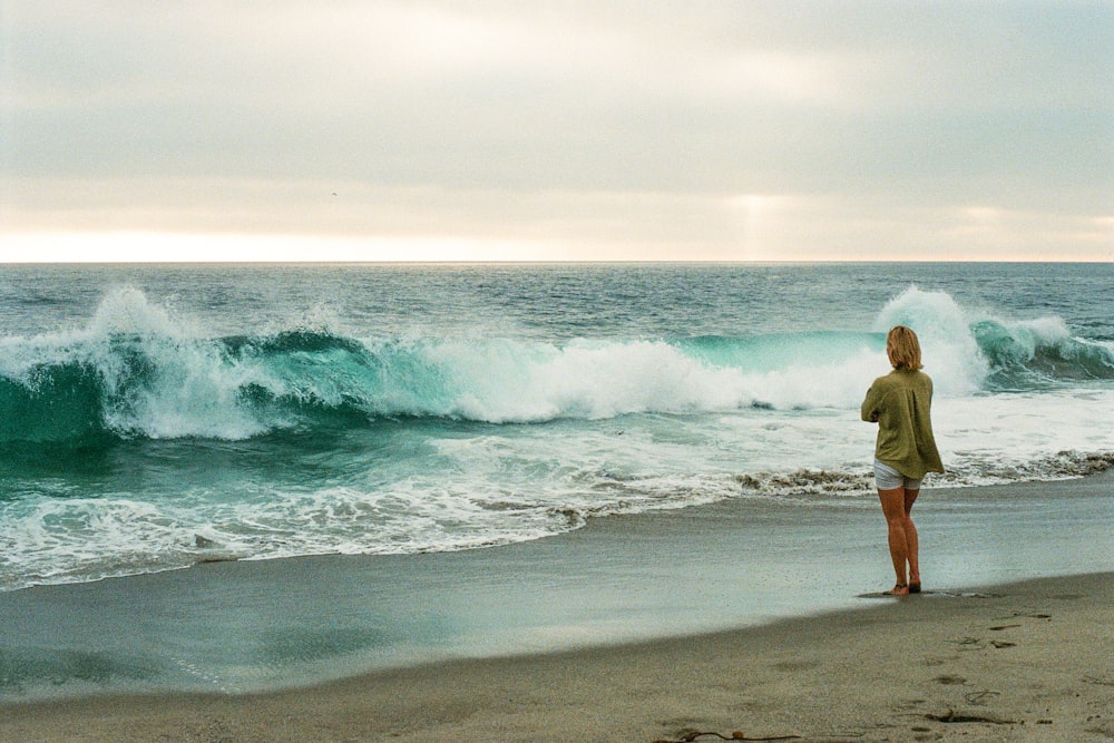 a person standing on a beach looking at waves crashing