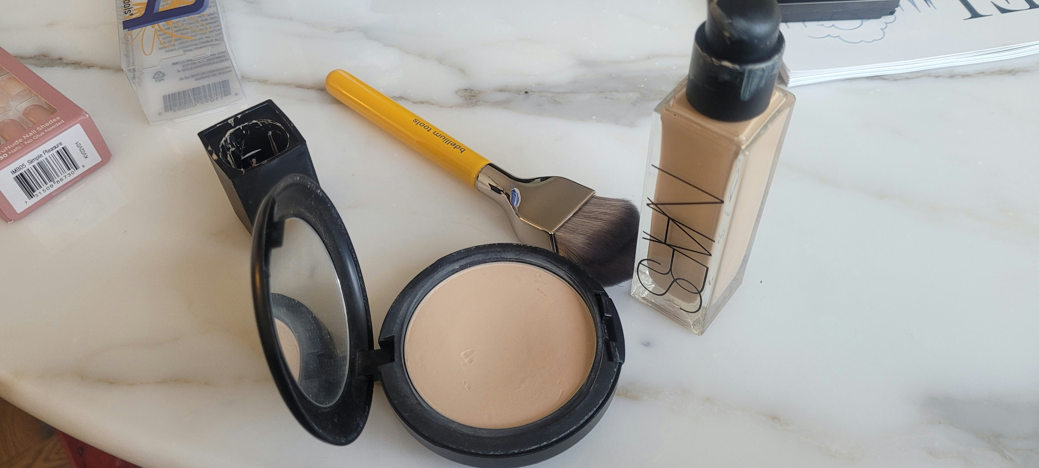 Cosmetic foundation bottles and brushes on white marble with soft lighting