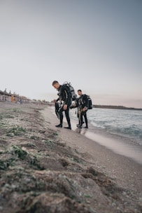 An instructor teaching a young diver how to use scuba gear on a sandy beach.