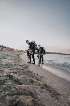 A friendly instructor guiding a student through scuba gear preparation on the beach.