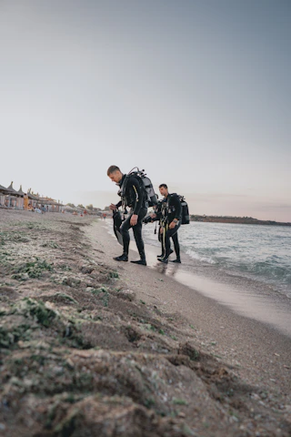A group of diverse beginner divers preparing their gear on a sunny beach.