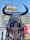 A massive mechanical sculpture of a bull with intricate metallic features and large horns stands prominently with a modern building in the background. The bull has a nose ring and chains hanging from its mouth, and its design is industrial and artistic.