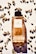 A bottle of D&G 11 La Force perfume is positioned in the center, surrounded by scattered cardamom pods on a white surface. The bottle is filled with an amber-colored liquid and features a black cap.