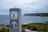 A signpost with the emblem of the National Parks & Wildlife Service is displayed prominently. The background reveals a coastal landscape with cliffs and the ocean under a cloudy sky.