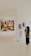 A person is standing in an art gallery, observing an exhibition. A large painting featuring several figures is displayed prominently on a white wall. Nearby, there are smaller black-and-white sketches. The gallery is well-lit, and the floor is polished.
