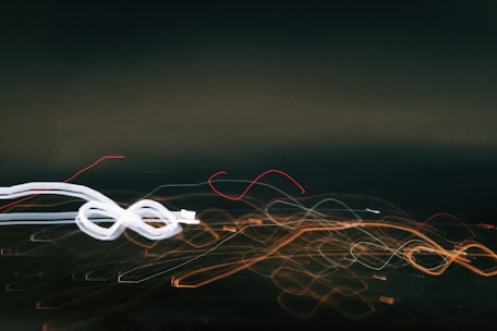 A dynamic array of colorful light trails curves and loops across a dark background, suggesting movement and speed. The lights vary in color from white and orange to red, creating an energetic scene.