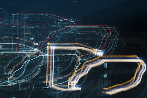 An abstract cityscape with vibrant light trails creating a pattern of lines and shapes against a dark background. The scene suggests movement and energy, as the lights are blurred and layered to form intricate designs.