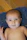 A cheerful baby in a cozy blue romper sitting on a colorful blanket indoors.