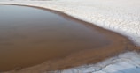 A small body of water is surrounded by a vast area of cracked, dry earth, indicating a drought-stricken landscape.