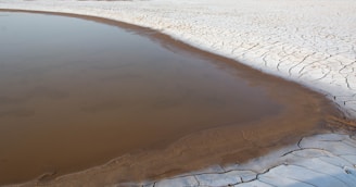 A small body of water is surrounded by a vast area of cracked, dry earth, indicating a drought-stricken landscape.