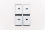 Four small framed photographs are arranged in a grid on a plain white wall. Each photograph features a landscape with water and a distant structure, possibly an island or mountain. The images are set in minimalistic black frames with a clean and modern aesthetic.