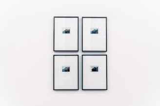 Four small framed photographs are arranged in a grid on a plain white wall. Each photograph features a landscape with water and a distant structure, possibly an island or mountain. The images are set in minimalistic black frames with a clean and modern aesthetic.