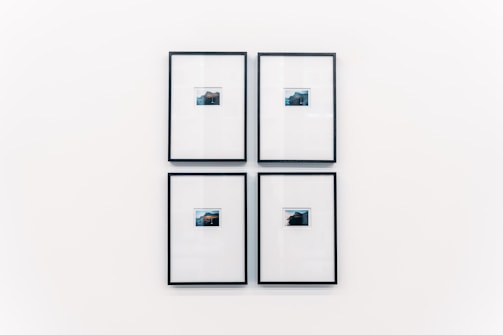 Four small framed photographs are arranged in a grid on a plain white wall. Each photograph features a landscape with water and a distant structure, possibly an island or mountain. The images are set in minimalistic black frames with a clean and modern aesthetic.