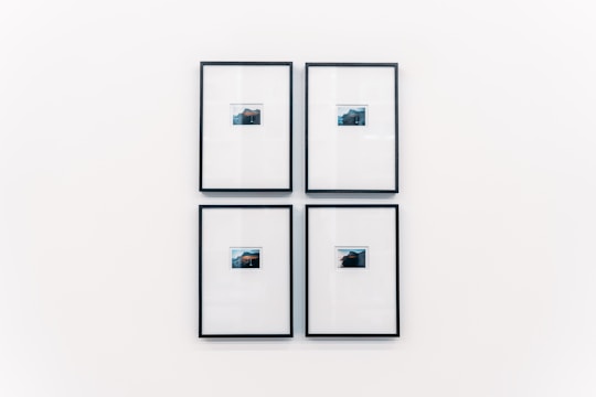 Four small framed photographs are arranged in a grid on a plain white wall. Each photograph features a landscape with water and a distant structure, possibly an island or mountain. The images are set in minimalistic black frames with a clean and modern aesthetic.
