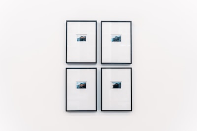 Four small framed photographs are arranged in a grid on a plain white wall. Each photograph features a landscape with water and a distant structure, possibly an island or mountain. The images are set in minimalistic black frames with a clean and modern aesthetic.
