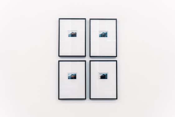 Four small framed photographs are arranged in a grid on a plain white wall. Each photograph features a landscape with water and a distant structure, possibly an island or mountain. The images are set in minimalistic black frames with a clean and modern aesthetic.