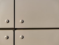 A close-up view of a section of a metal surface, featuring four screws with evenly spaced, flat panels. The panels are a light tan color with a slightly reflective finish, and they are arranged in a grid with visible seams.